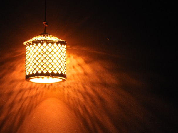 Golden metal Moroccan lantern casting delicate shadows on a minimalist black wall.