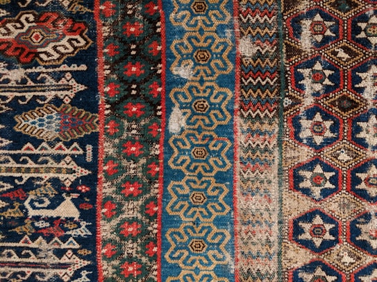 An intricately designed textile with a geometric pattern featuring a variety of shapes including hexagons and diamonds. The design is composed of vibrant colors and is divided into distinct vertical sections, each with unique patterns.