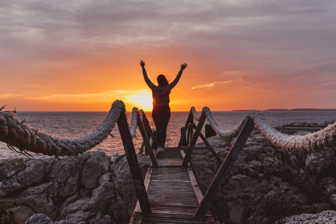 woman standing on a wooden bridge fronting the sea during golden hour