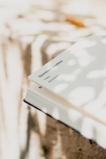 An open book lies on a surface, with sunlight casting dappled shadows across its pages. The page visible appears to contain the heading 'Sermon Notes' in bold text.