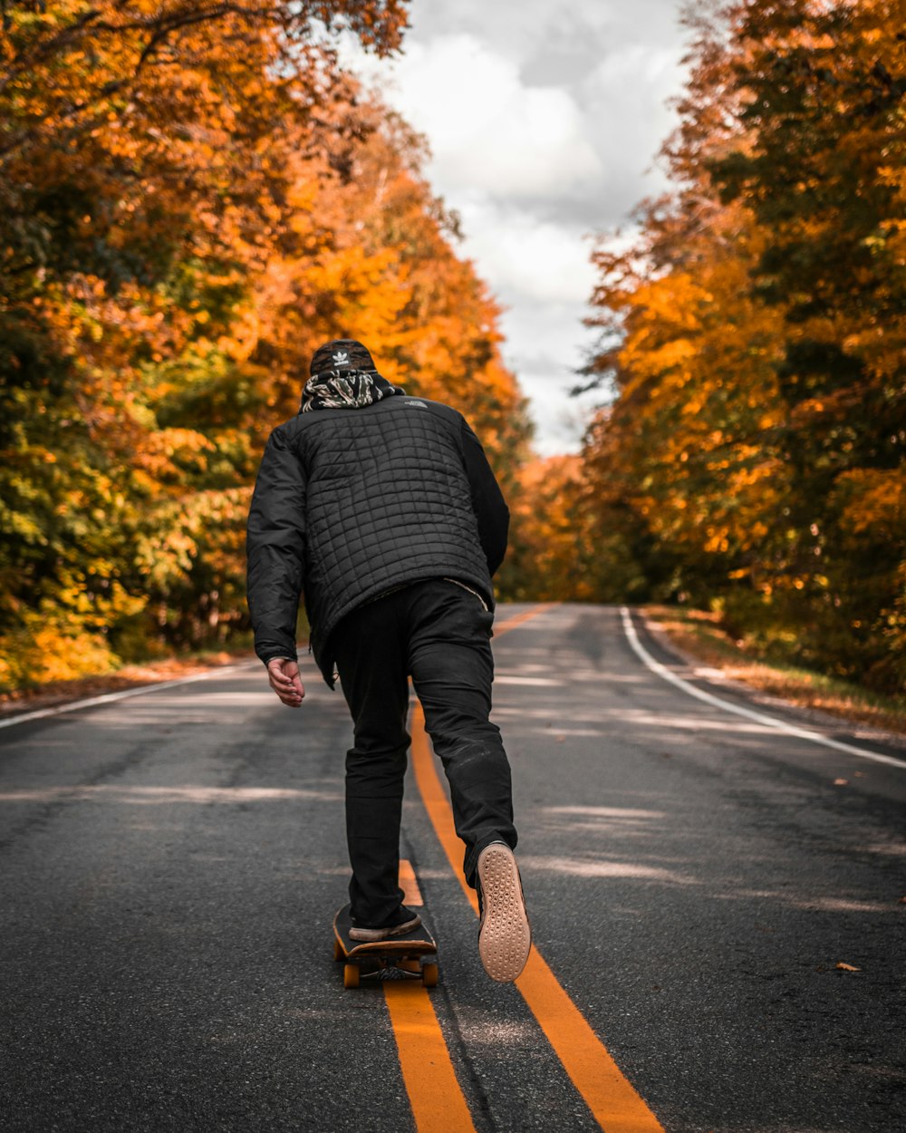 Homem na jaqueta preta patinando na estrada entre árvores amarelas
