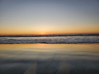 A warm, inviting photo of a sunset over the Cabo San Lucas arch with calm sea waters.
