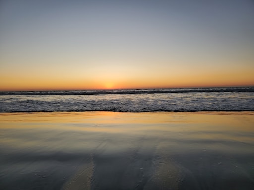 A warm, inviting photo of a sunset over the Cabo San Lucas arch with calm sea waters.