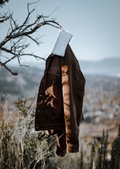 A cozy fleece-lined jacket displayed on a hanger with snow-covered pine branches in the background.