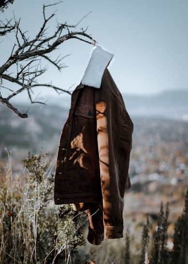 A sleek, insulated men's jacket hanging outdoors with light snow falling softly in the background.