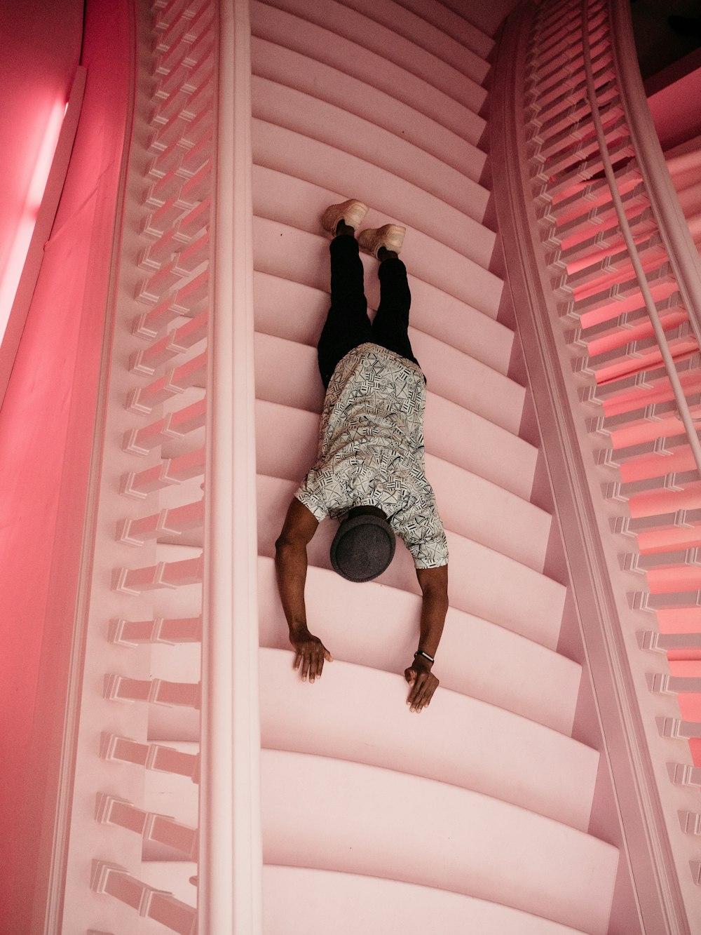 man wearing black and white crew-neck shirt and black pants laying on pink concrete stairs