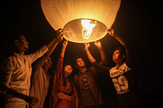 A group of diverse community members gathered around a glowing lantern in a park at dusk.