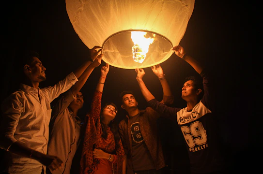 A group of diverse community members gathered around a glowing lantern in a park at dusk.