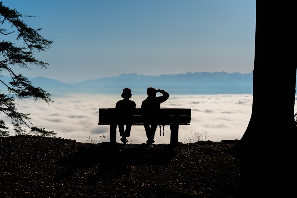 two persons sitting on a bench overlooking a sea of clouds