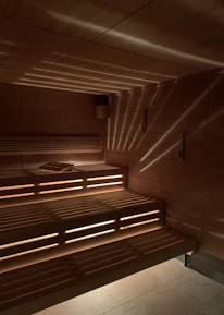 A wooden sauna with tiered seating is depicted, featuring warm lighting that casts a patterned glow on the walls and ceiling. A towel is placed on one of the benches.
