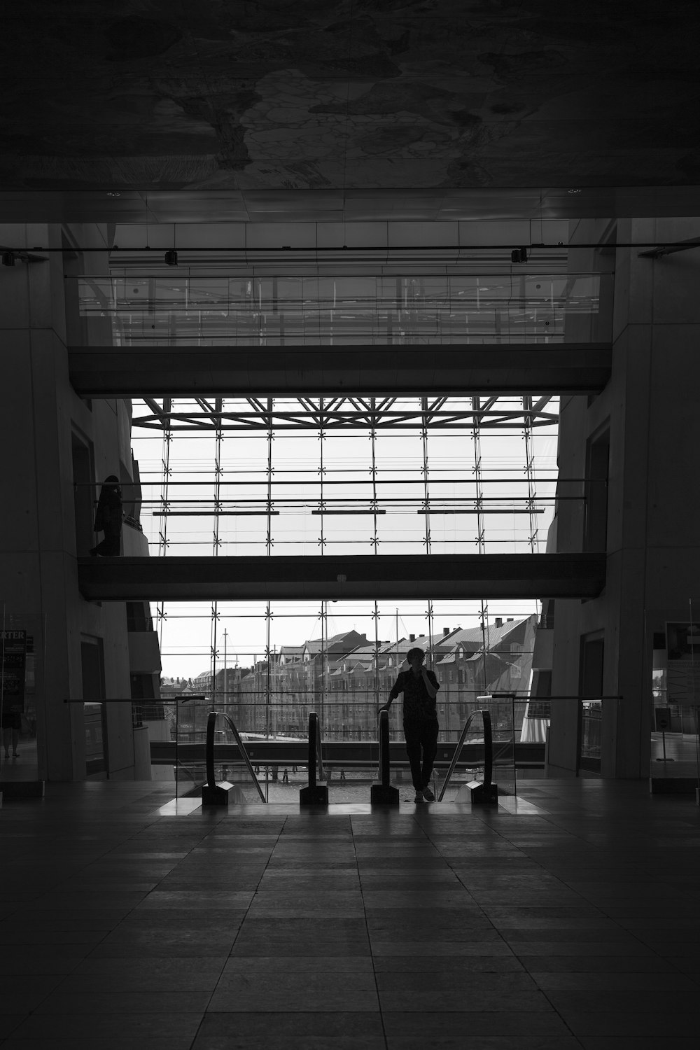 grayscale photo of man standing in front of glass windows
