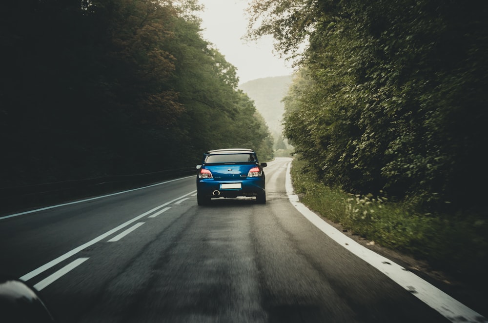 blue car passing by an asphalt road