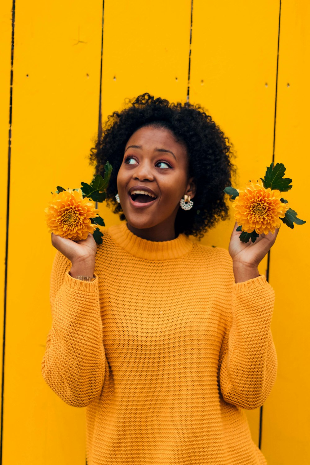 woman standing beside yellow wall while holding yellow flowers