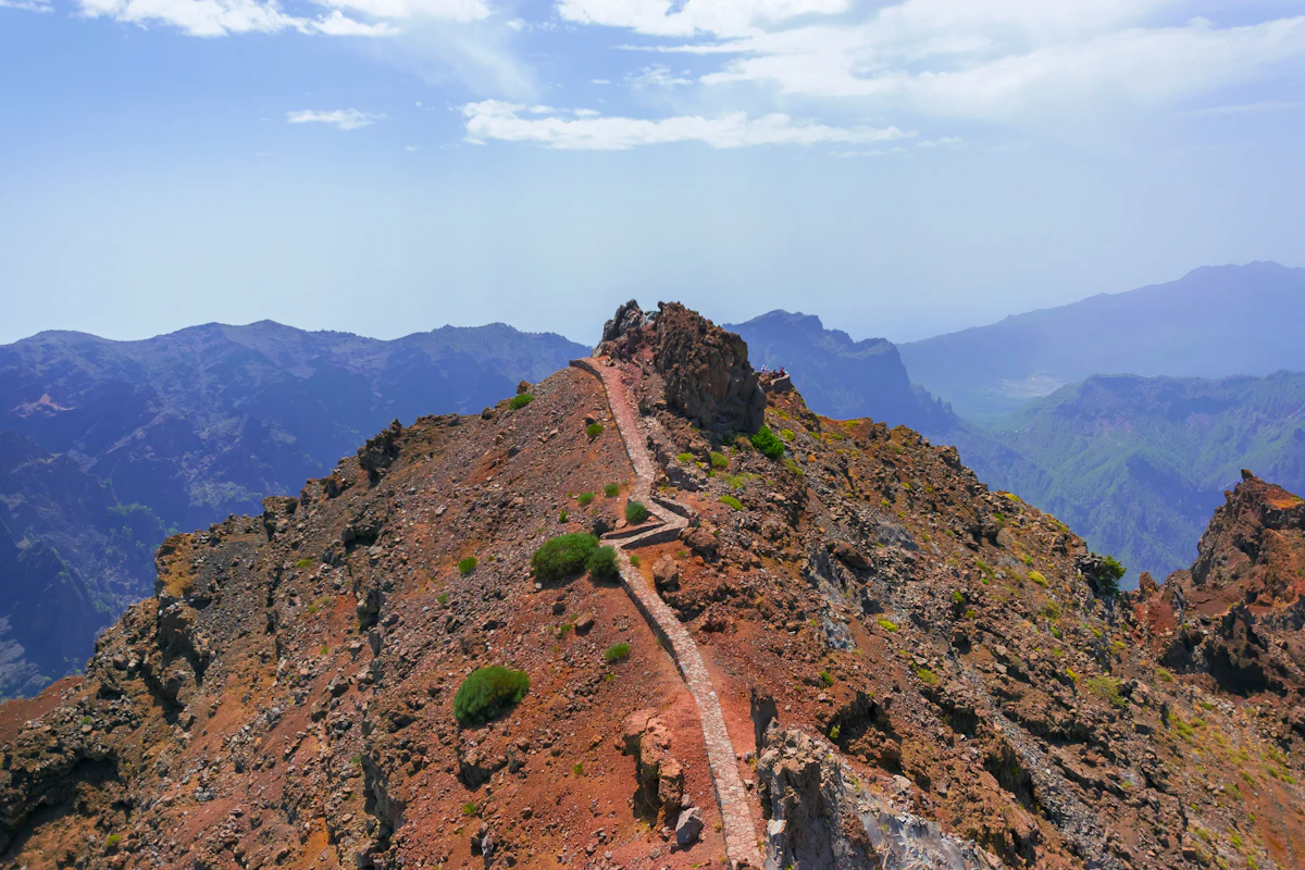 A stone path along a narrow rocky ridge at Roque de los Muchachos, with mountain ridges behind