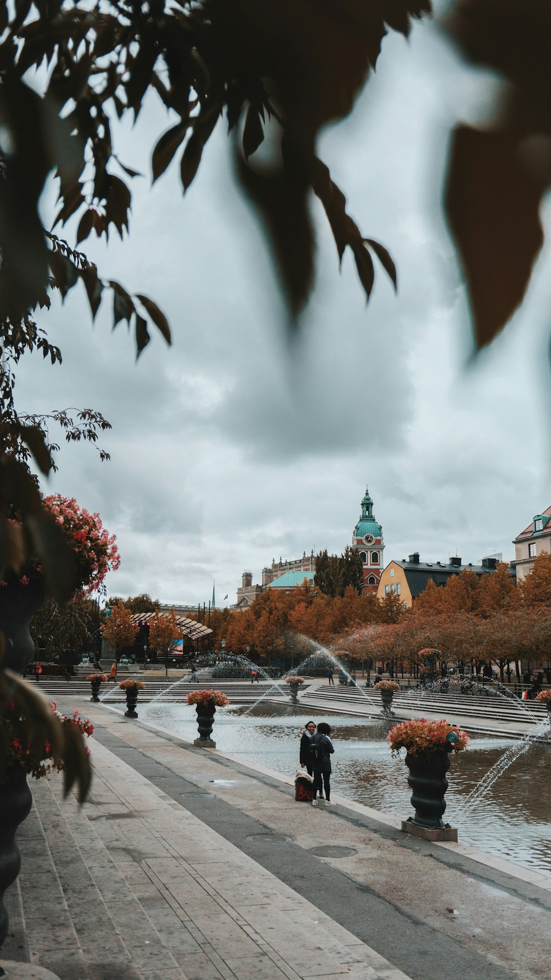 two people standing beside water fountain at daytime photo two people standing beside water fountain at daytime photo