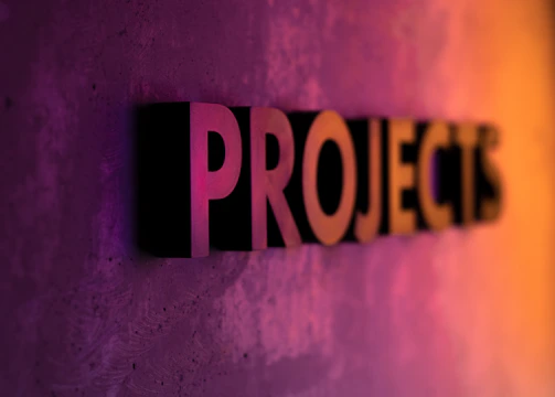 The word 'PROJECTS' appears in large, bold, three-dimensional letters against a textured surface, with vibrant lighting that transitions from purple to orange, creating a dynamic gradient effect.