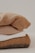 A neatly stacked pile of knitted sweaters in various shades, including cream, tan, and brown. The texture of the fabric is clearly visible, suggesting warmth and coziness.