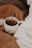 A cozy setup featuring a polka-dotted ceramic mug filled with tea or a hot beverage, nestled among soft, knitted blankets in various shades of brown and white. A metallic tea infuser sticks out of the mug, suggesting a freshly brewed drink.