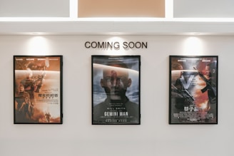 Three framed movie posters are displayed on a wall beneath the text 'COMING SOON.' The central poster features the title 'Gemini Man,' while the other two posters are in another language and contain action-themed imagery.