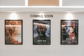 Three framed movie posters are displayed on a wall beneath the text 'COMING SOON.' The central poster features the title 'Gemini Man,' while the other two posters are in another language and contain action-themed imagery.