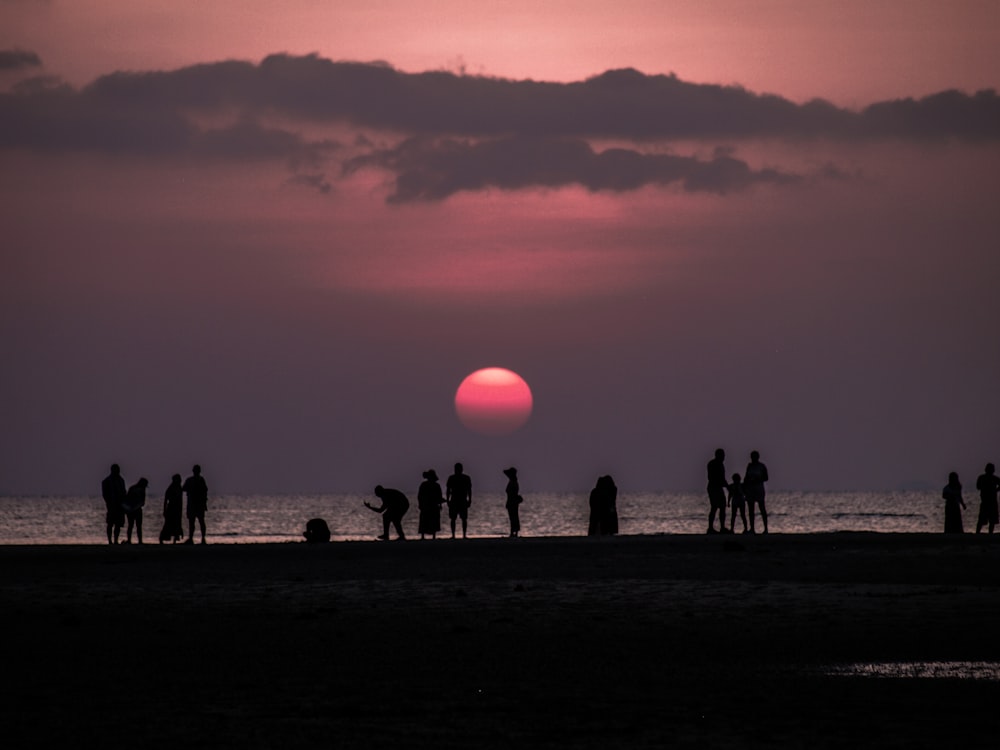 people standing near seashore showing full moon during night time