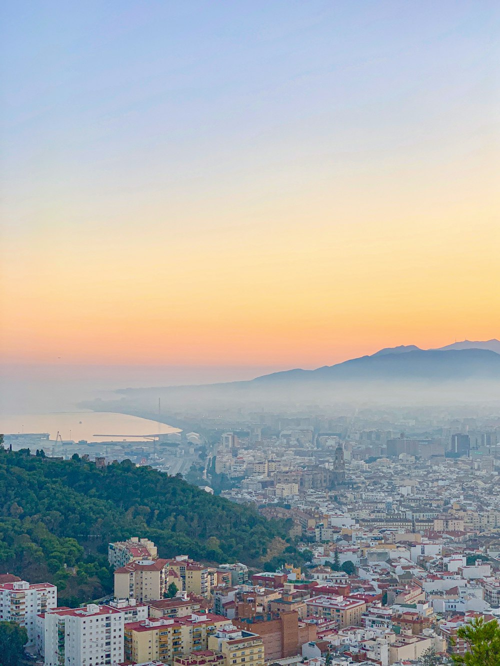 Fotografía aérea de la ciudad con edificios de gran altura que ven la montaña bajo el cielo amarillo durante el día