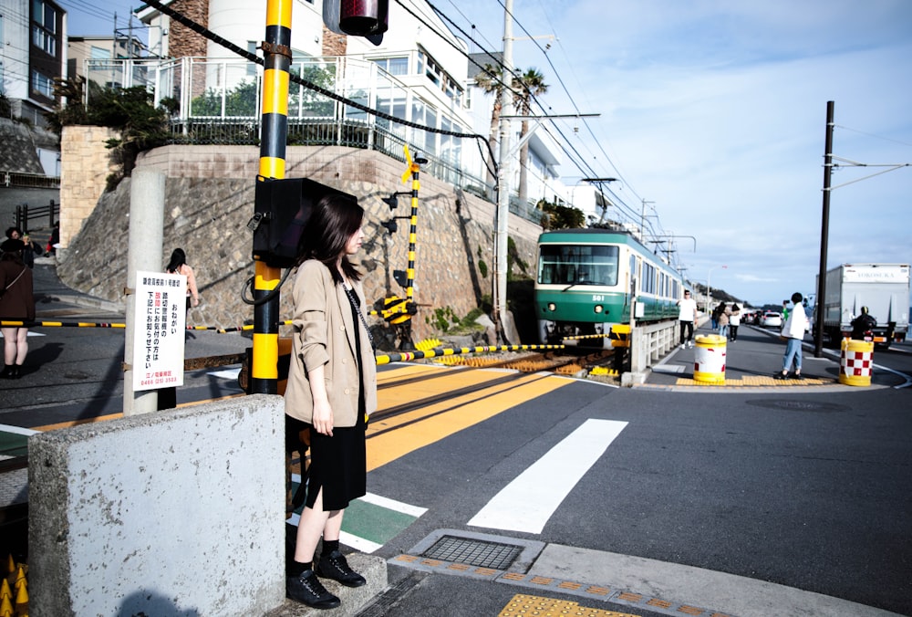 woman standing near road viewing train and buildings under white and blue sky during daytime