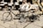 A collection of traditional drums and colorful painted musical instruments is displayed on a cobblestone surface. Two small decorative bicycles are positioned in the foreground, with intricate designs and patterns adorning their frames. The background is filled with various types of drums, including some with vibrant motifs and designs.
