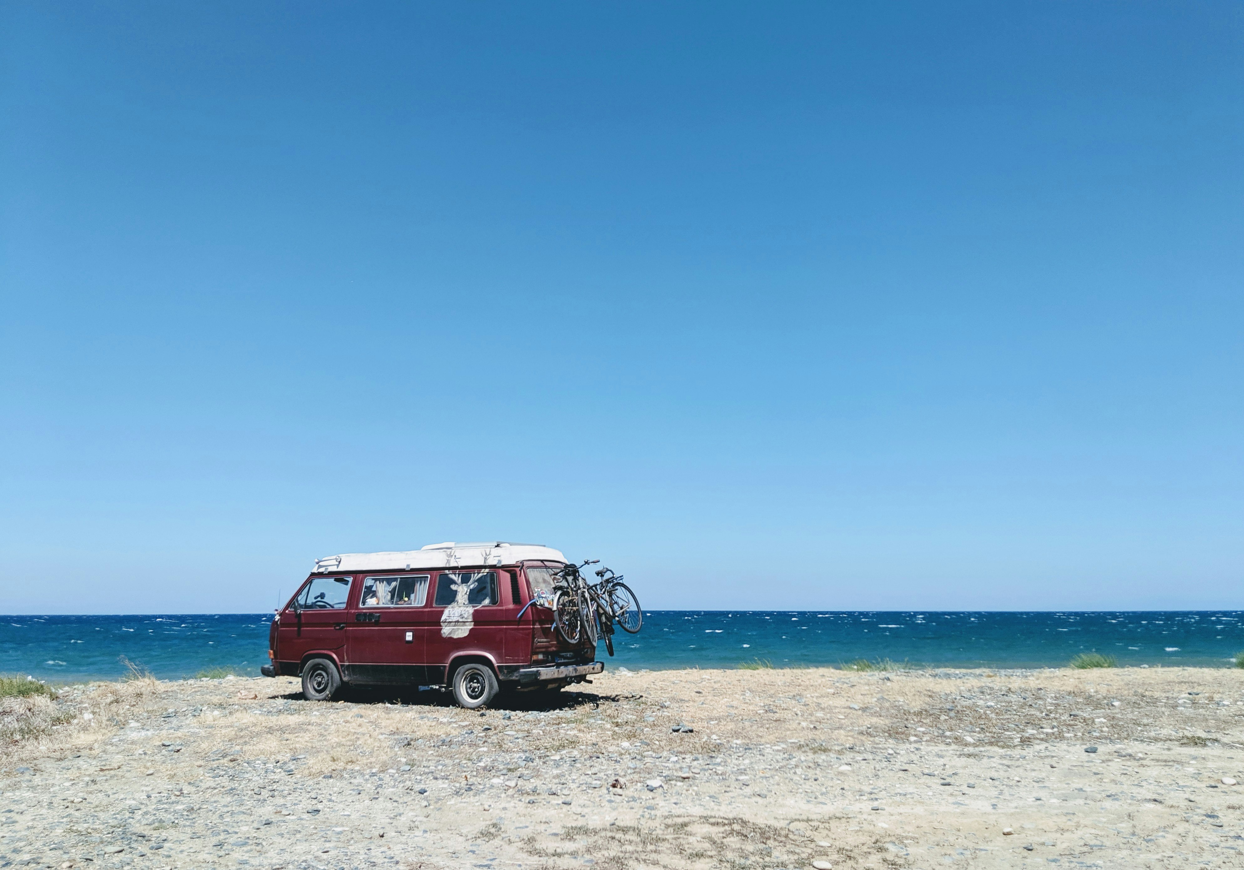 red van near seashore viewing blue sea during daytime