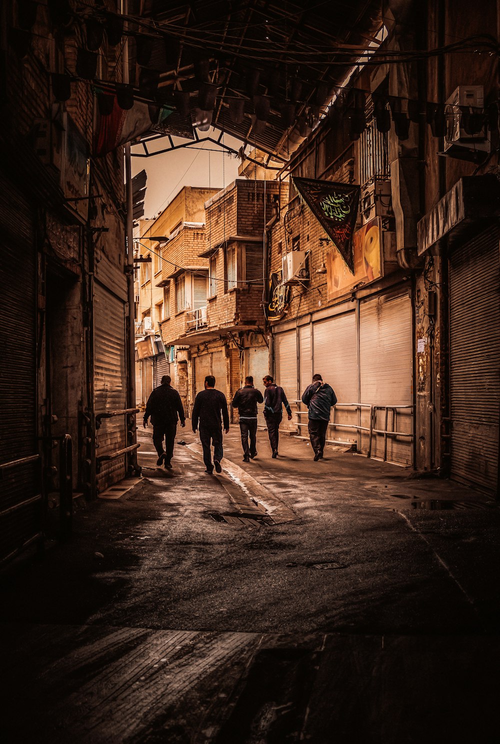 five men walking on the pathway in between of buildings