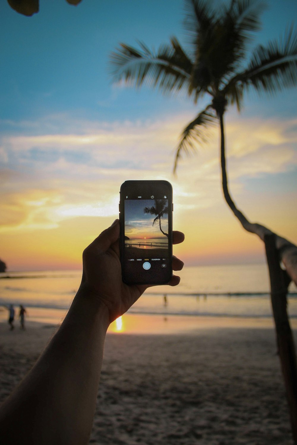 person holding smartphone displaying camera with body of water during golden hour