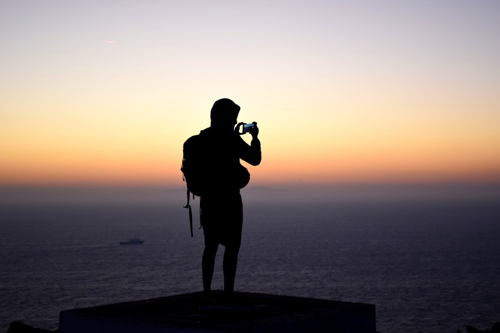 Silhouettenfotografie einer Person, die während der goldenen Stunde vor einem ruhigen Gewässer steht