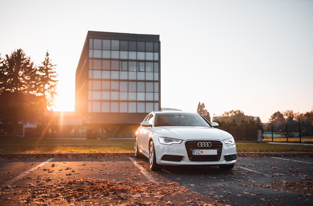 Audi sedan branco estacionado em área de estacionamento de concreto cercado por folhas secas