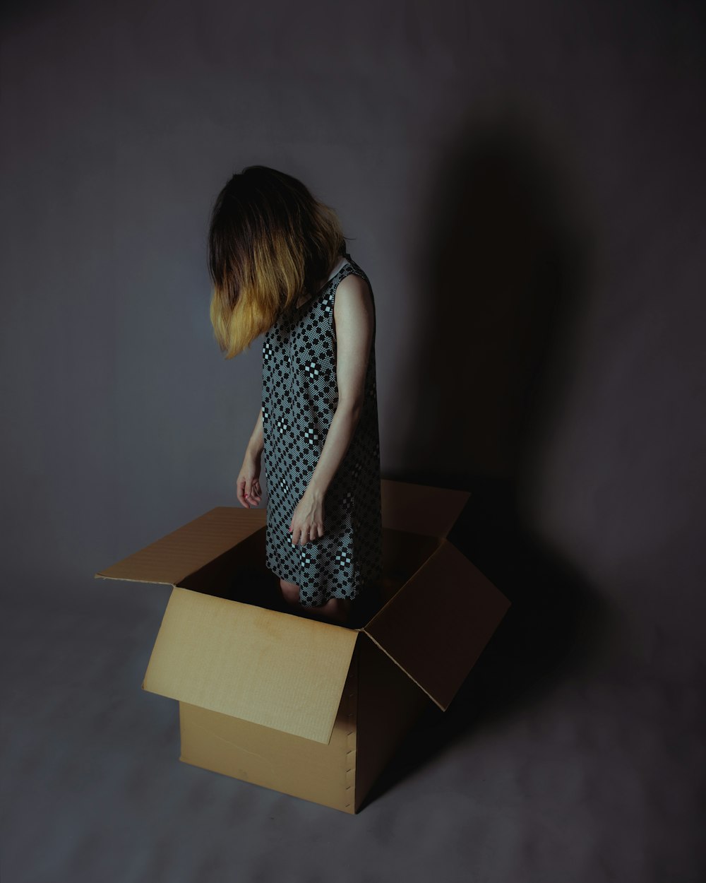 fille portant une robe sans manches grise et blanche debout sur une boîte en carton