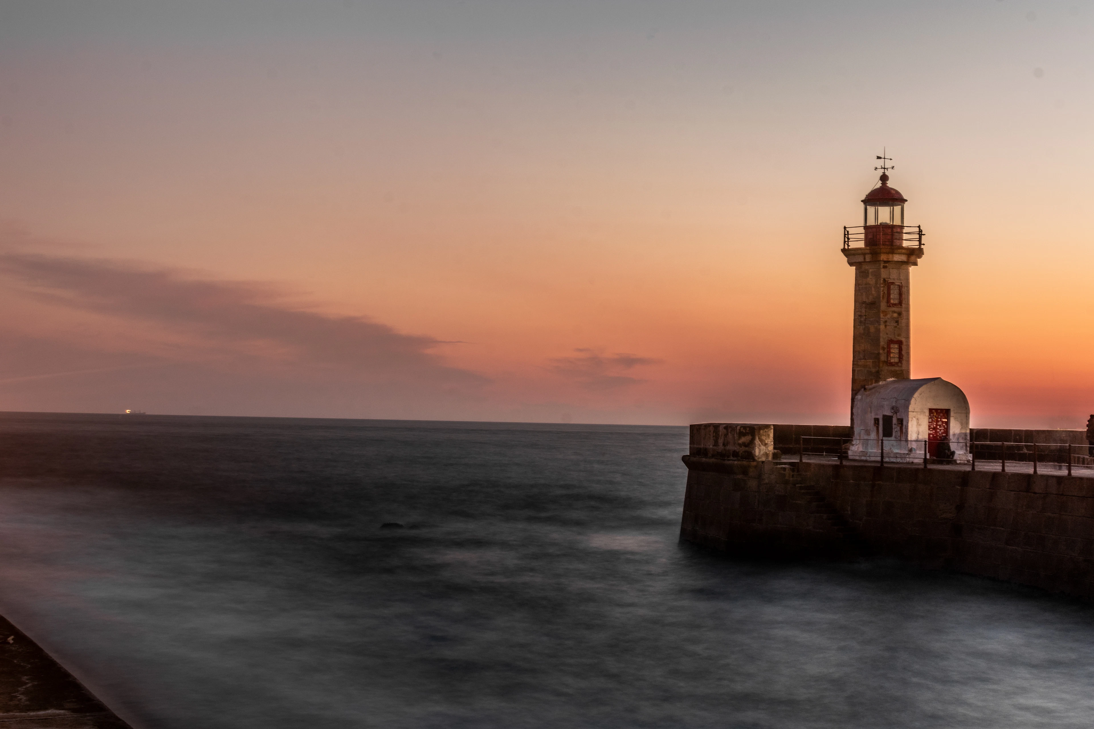 The Felgueiras lighthouse at the end of its stone pier in Foz do Douro, Porto, standing against an orange and violet sunset with the Atlantic smoothed to silk by a long exposure.