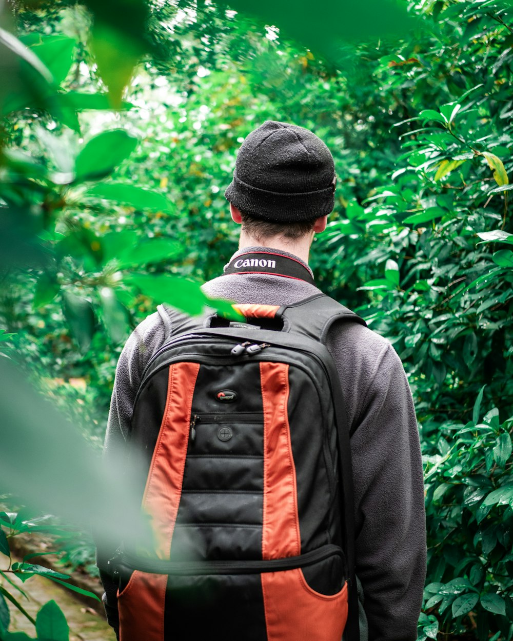 man in black jacket with backpack beside plants
