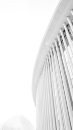Curved lines and vertical columns create a modern architectural design with a minimalist aesthetic. The structure is sleek and futuristic, composed mostly of light colors, enhancing the clean and simple lines.