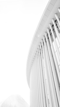 Curved lines and vertical columns create a modern architectural design with a minimalist aesthetic. The structure is sleek and futuristic, composed mostly of light colors, enhancing the clean and simple lines.