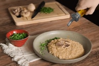 A rustic wooden table set with a steaming bowl of creamy mushroom risotto garnished with parsley.