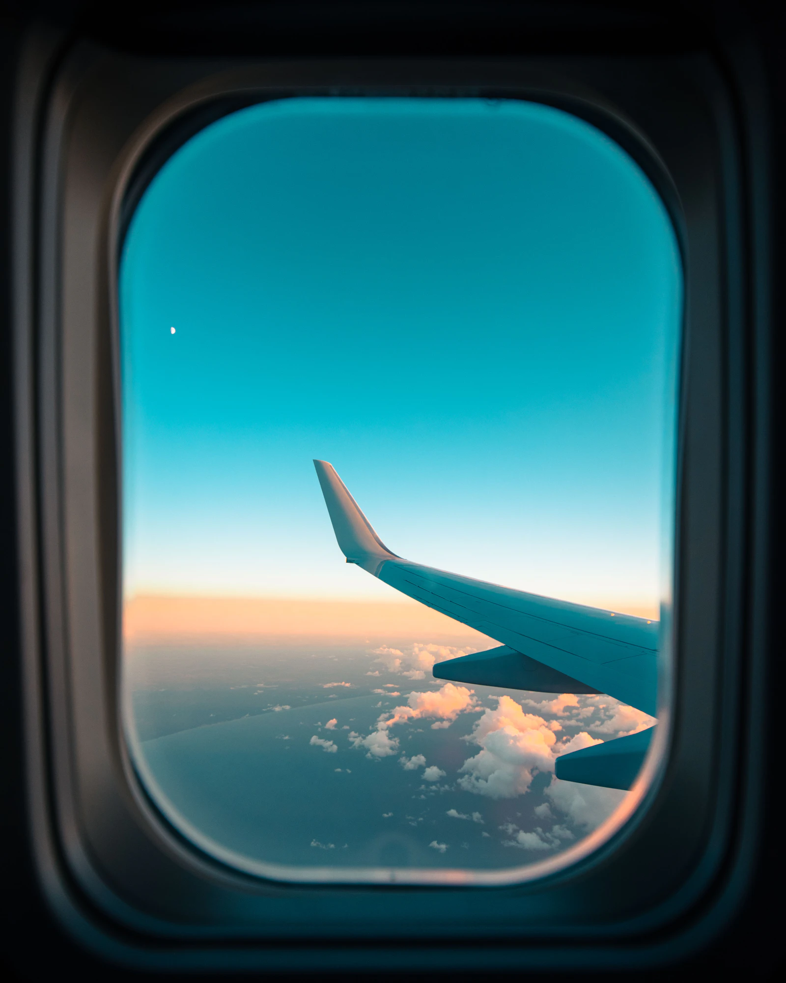 Airliner wing seen through a cabin window above a blanket of clouds during a smooth daytime flight