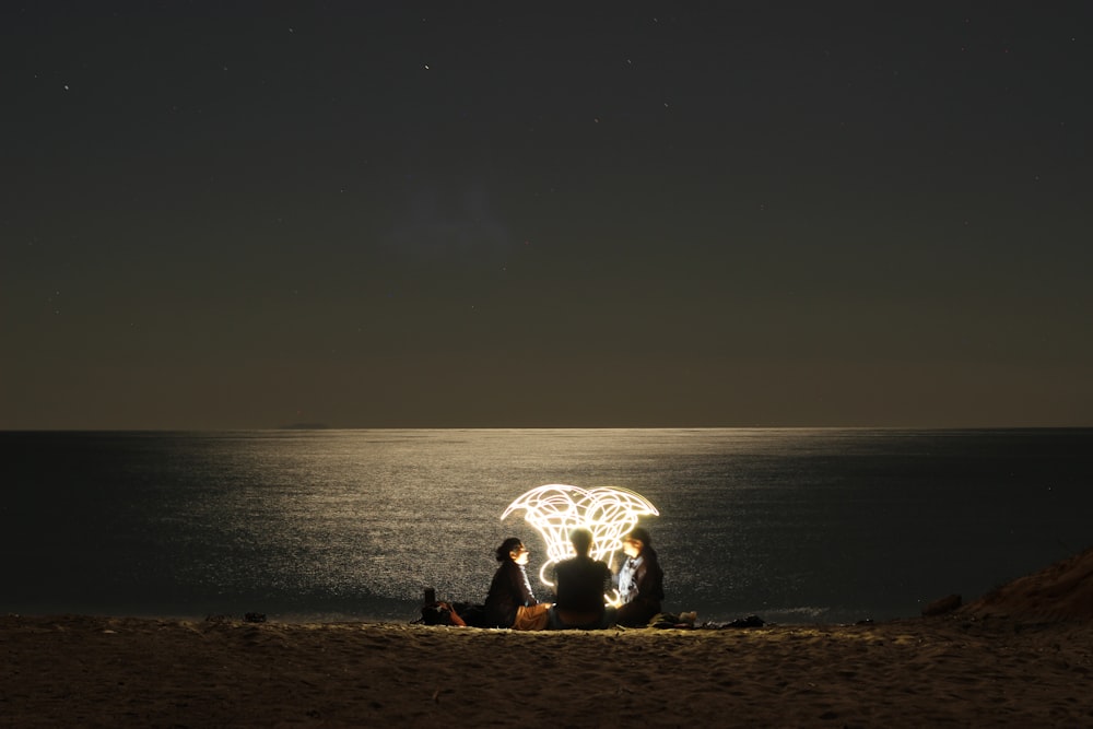 three person on seashore at night