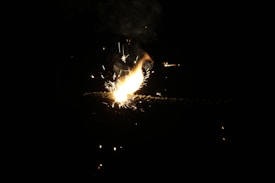 Sparks and bright flames are emitted from the burning tip of a firecracker against a dark background, creating an intense and dynamic visual effect.