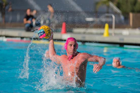 A focused young female athlete practicing water polo shots in a sunlit pool.