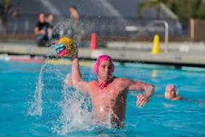 A player mid-throw, water splashing as the ball arcs toward the goal.