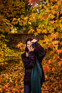 A friendly photographer capturing candid moments of a smiling senior student outdoors with vibrant fall leaves in the background.