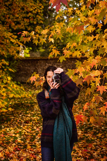 A friendly photographer capturing candid moments of a smiling senior student outdoors with vibrant fall leaves in the background.