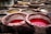 Circular stone vats filled with various colored liquids, predominantly red and yellow, set in a traditional tannery environment. The vats have tiled interiors and are used for dyeing or tanning processes.