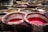 Circular stone vats filled with various colored liquids, predominantly red and yellow, set in a traditional tannery environment. The vats have tiled interiors and are used for dyeing or tanning processes.