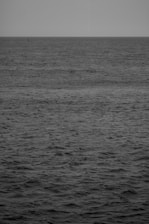 Minimalist black and white image of a camera lens reflecting the horizon over the ocean.