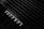 A close-up view of a Ferrari logo on a sleek, black surface with a grille-like pattern in the background. The composition highlights the luxury branding and design details, with an emphasis on texture and contrast.